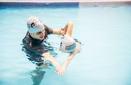 Male swimming instructor training a young student in-water